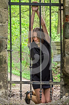 Young beautiful girl prisoner behind an iron fence