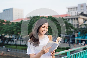 Young beautiful girl reading book on a bridge with city view