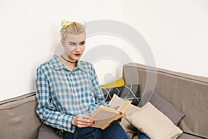 Young beautiful girl reading book sitting on sofa in the room