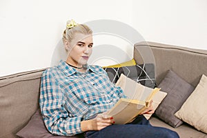 Young beautiful girl reading book sitting on sofa in the room