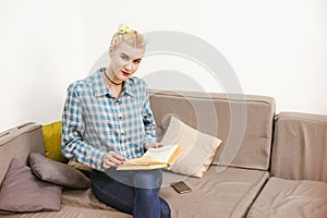 Young beautiful girl reading book sitting on sofa in the room