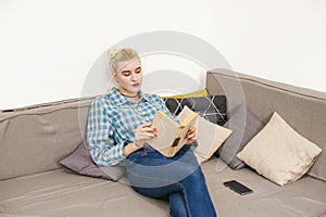 Young beautiful girl reading book sitting on sofa in the room