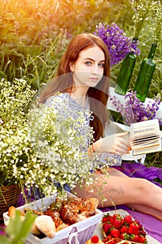 Young beautiful girl reads a book in nature sitting, where there are a lot of flowers and grass. Nature and relaxation. Leisure