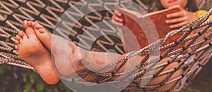 Young beautiful girl reads a book outdoors in a hammock.  Selective focus. Horizontal image