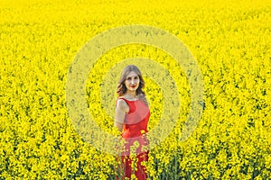 Young beautiful girl in a red dress close up in the middle of the yellow field with the radish flowers closeup