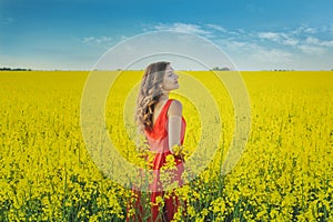 Young beautiful girl in a red dress close up in the middle of the yellow field with the radish flowers closeup