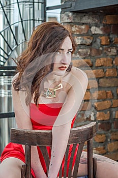 Young beautiful girl in a red dress is sitting on a wooden chair in a cafe on a street in the city of Lviv