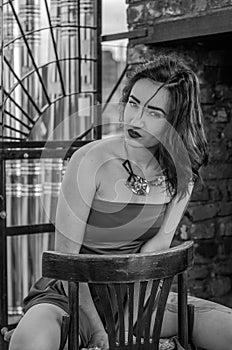 Young beautiful girl in a red dress is sitting on a wooden chair in a cafe on a street in the city of Lviv