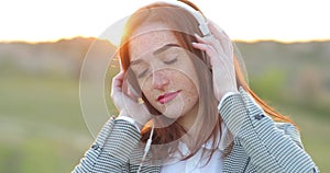 Young beautiful girl with red hair listening to music smartphone, happy face, outdoor hipster portrait on the nature