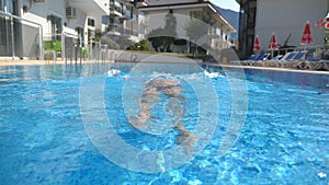 Young beautiful girl relaxing in pool at warm sunny day. Woman swimming on the back. Summer vacation holiday concept