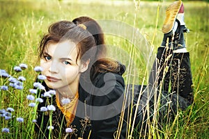 A young beautiful girl is resting in the summer in a field with flowers. the brunette is lying in the green grass..