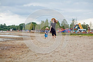 A young beautiful girl runs along a sandy beach in the sea with her son