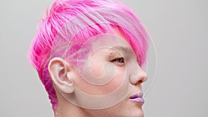 Young beautiful girl with a short haircut and pink hair. A homosexual lesbian model poses on a white background.