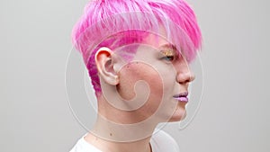 Young beautiful girl with a short haircut and pink hair. A homosexual lesbian model poses on a white background.