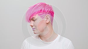 Young beautiful girl with a short haircut and pink hair. A homosexual lesbian model poses on a white background.