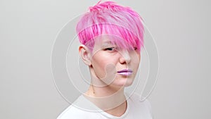 Young beautiful girl with a short haircut and pink hair. A homosexual lesbian model poses on a white background.