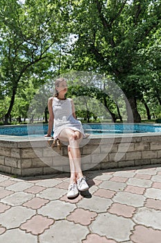 Young beautiful girl in short white dress sit near fountain