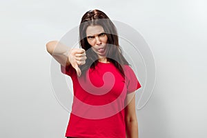 Young, beautiful girl showing a gesture with her hands thumbs down. Isolated on a light background. Different human emotions,