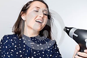 Young beautiful girl singing with hairdryer, woman feeling happy, drying her hair with dryer