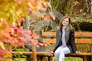 A young beautiful girl sits on a bench in an autumn park