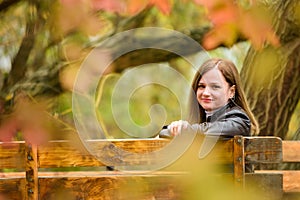 A young beautiful girl sits on a bench in an autumn park and turns around and looks into the frame.
