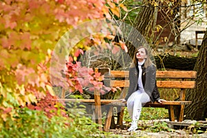 A young beautiful girl sits on a bench and enjoys the autumn landscape
