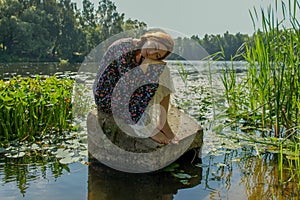 A young beautiful girl sits on a stone in the middle of a lake and dreams.