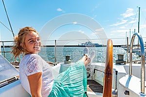 Young beautiful girl sits on a yacht near the helm in the sea and looks at the camera on the deck.