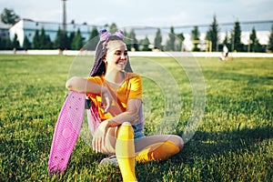 Young beautiful girl sitting on a lawn holding a skateboard in her hand in a yellow T-shirt and yellow socks in the open