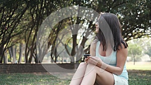 Young Beautiful Girl Sitting On Lawn In Park Using Phone, On-line Shopping Concept