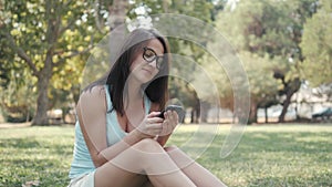 Young Beautiful Girl Sitting On Lawn In Park Using Phone, On-line Shopping Concept