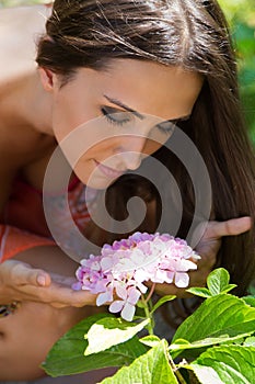 Young beautiful girl smells flowers, against green summer garden