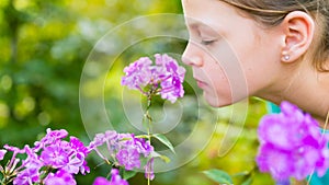 Young beautiful girl smells purple flowers in the garden