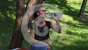 Young beautiful girl smiles and enjoys drinking water from a plastic bottle.