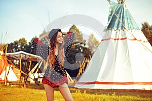 Young beautiful girl smiling on background teepee, tipi- native indian house. Pretty girl in hat with long cerly hair