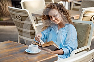 Young beautiful girl smiling, reading book, sitting in cafe.