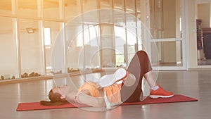 Young beautiful girl in sports clothes doing warm-up on the rug in the gym with tape