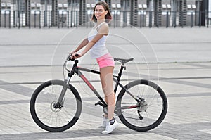 Young beautiful girl in sportswear stands next to a bicycle on the street in the city