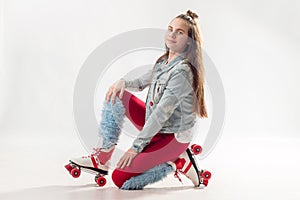 Young beautiful girl in sporty stylish clothes with long hair on four-wheeled rollers isolated on background