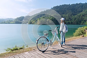 Young beautiful girl stand near a bicycle to looking at the view on bike trail at the lake in the morning. Active people. Outdoors