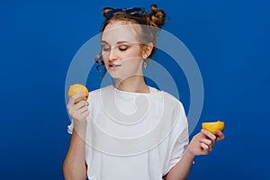 A young beautiful girl standing on a blue background holding lemons in her hand and biting