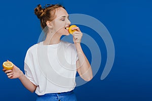 A young beautiful girl standing on a blue background holding lemons in her hand and biting