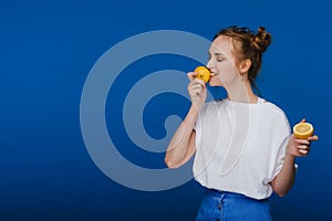 A young beautiful girl standing on a blue background holding lemons in her hand and biting