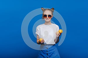 A young beautiful girl standing on a blue background holding lemons in her hand. Smiles