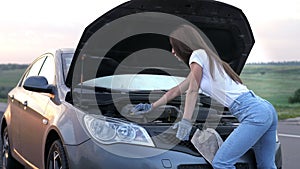 A young beautiful girl is standing by a broken car on the highway at sunset and calls the car service. The girl is