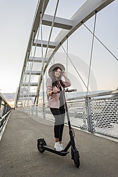 A young woman standing on the bridge next to her electric scooter