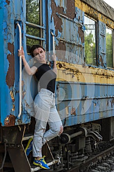 A young beautiful girl is standing on the step of an old railway carriage, a departing train