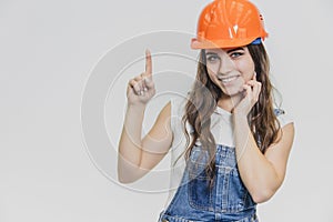 A young beautiful girl stands on a gray background. It is dressed in an orange helmet on the head. During this, he looks