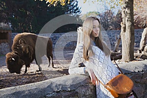 Young beautiful girl stands near the aviary with bison in city z