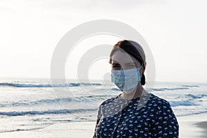 Young beautiful girl stands near the sea in a medical mask